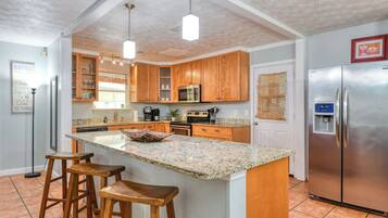 A kitchen with wooden cabinets, a granite countertop, a stainless steel refrigerator, and a coffee maker.