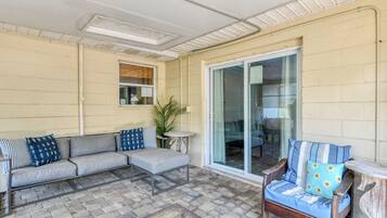 A covered patio area with a grey sofa, a wooden chair, and a small table.