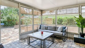 A covered patio area with a wooden table, a cushioned bench, and a potted plant.