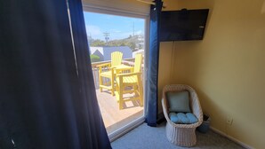 A room with a sliding glass door leading to an outdoor deck with yellow chairs and a wicker chair. - Ocean Side Beach Condo in Family Friendly Community!  Oceanfront pool!! (Pine Knoll Shores)