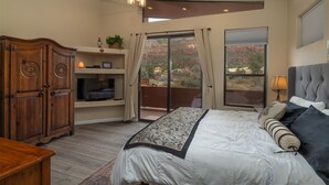 Quarto com uma cama grande, ventoinha no teto, TV em uma prateleira e vista para uma paisagem montanhosa por uma porta de correr.
