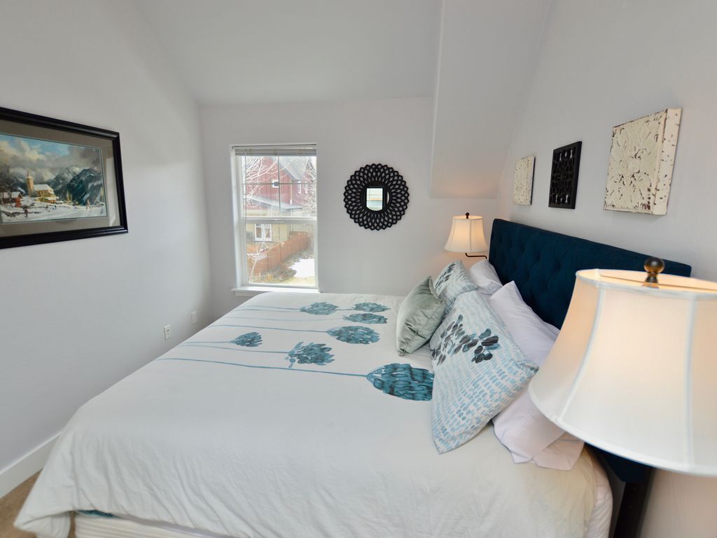 A bedroom with a bed, a window, a wall-mounted lamp, and artwork.