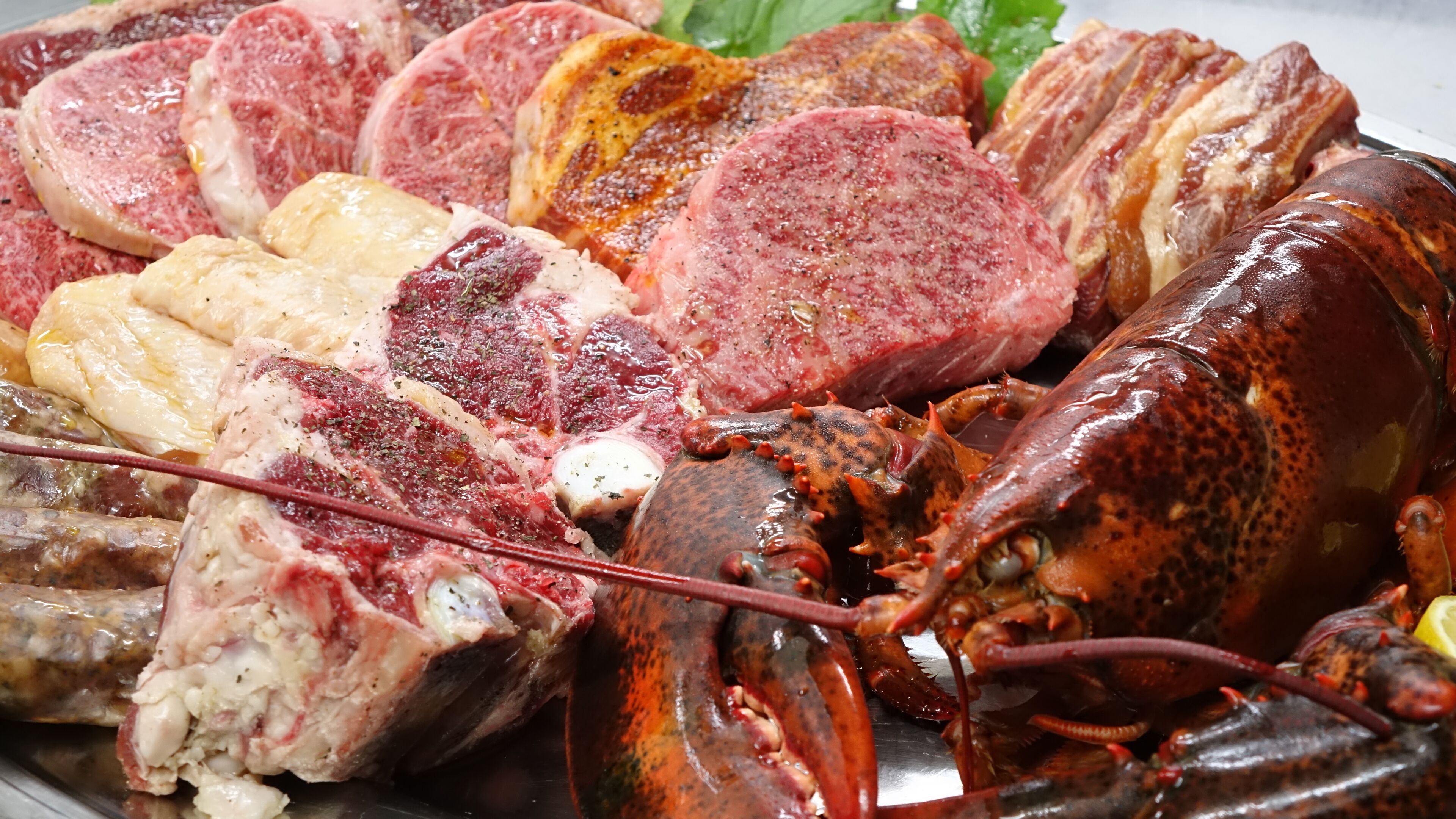 Variedad de carnes, incluyendo filetes, salchichas y langosta.