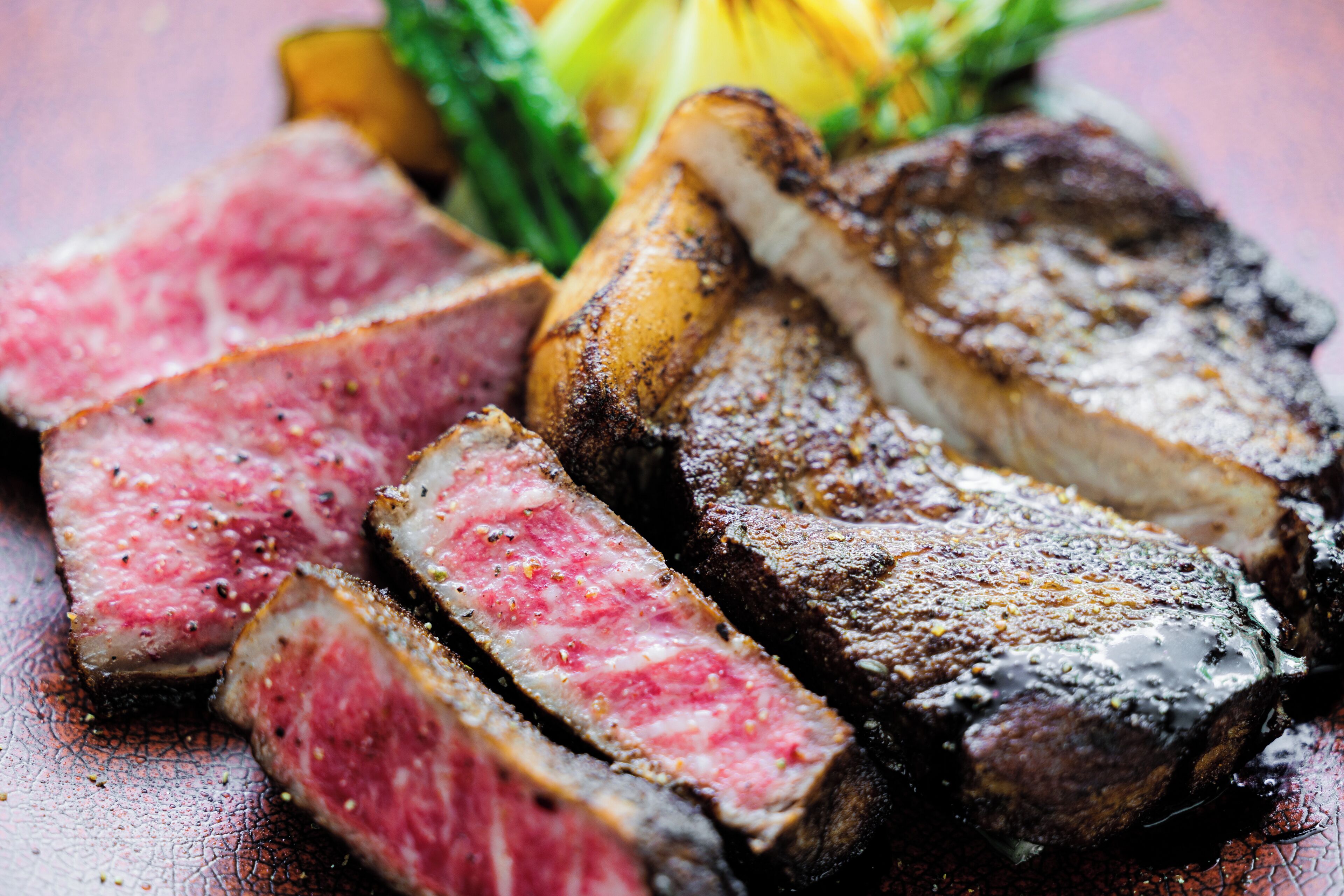 A close-up of a steak with a pink center, accompanied by grilled vegetables and a lemon wedge.