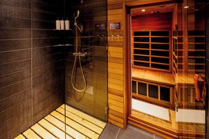 Un baño moderno con ducha de vidrio, suelo de madera y un reloj digital.