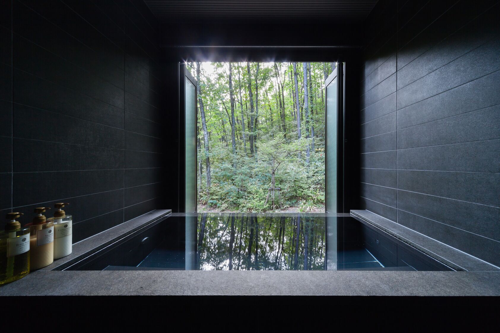 A modern bathroom with a glass enclosure, a bathtub, and toiletries on the counter.