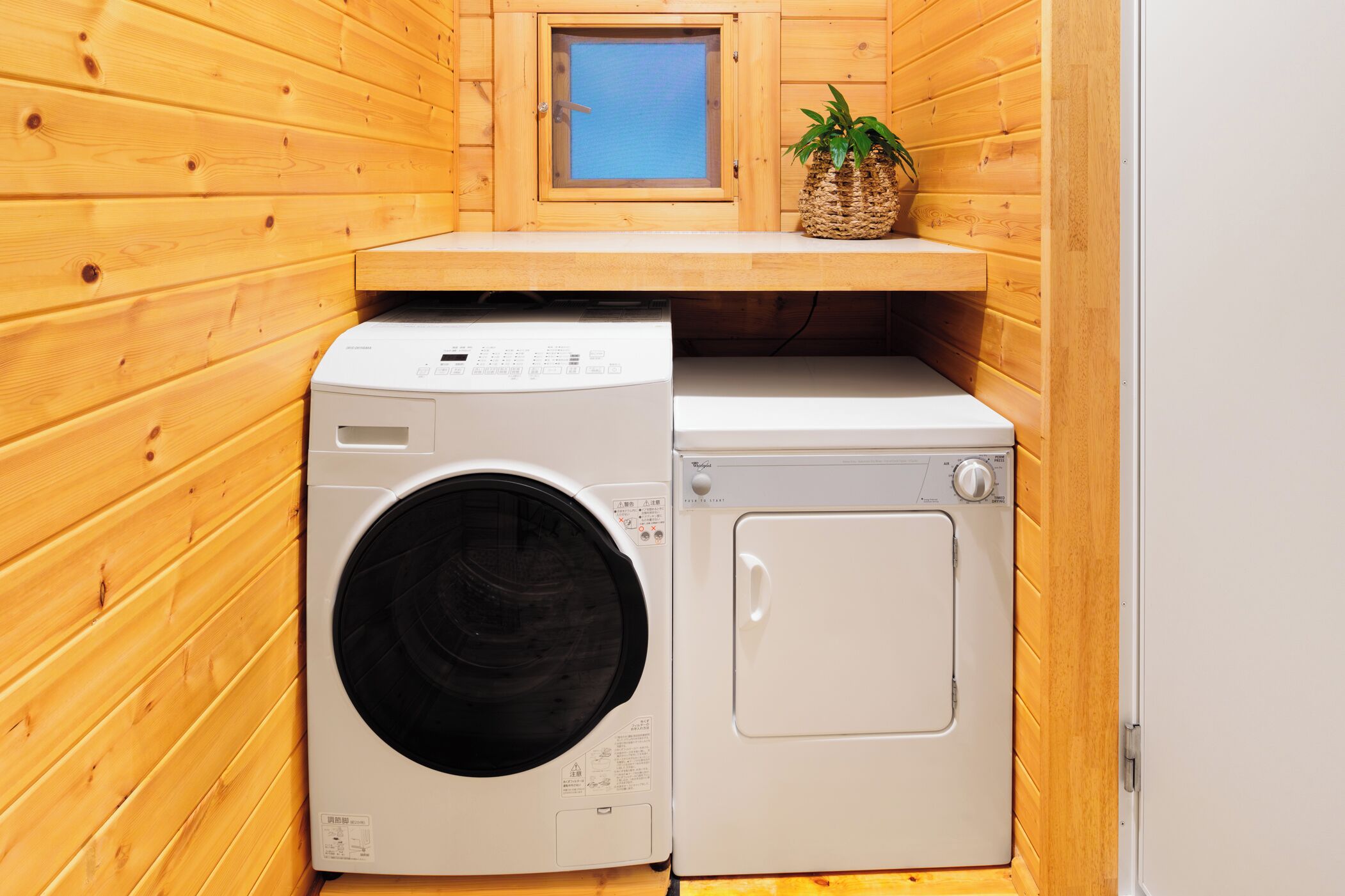 A compact laundry room with wooden walls, a washing machine, a dryer, and a small window with a view.