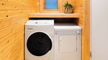 A compact laundry room with wooden walls, a washing machine, a dryer, and a small window with a view.