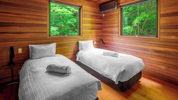 A room with two beds, wooden walls, and large windows with a forest view.