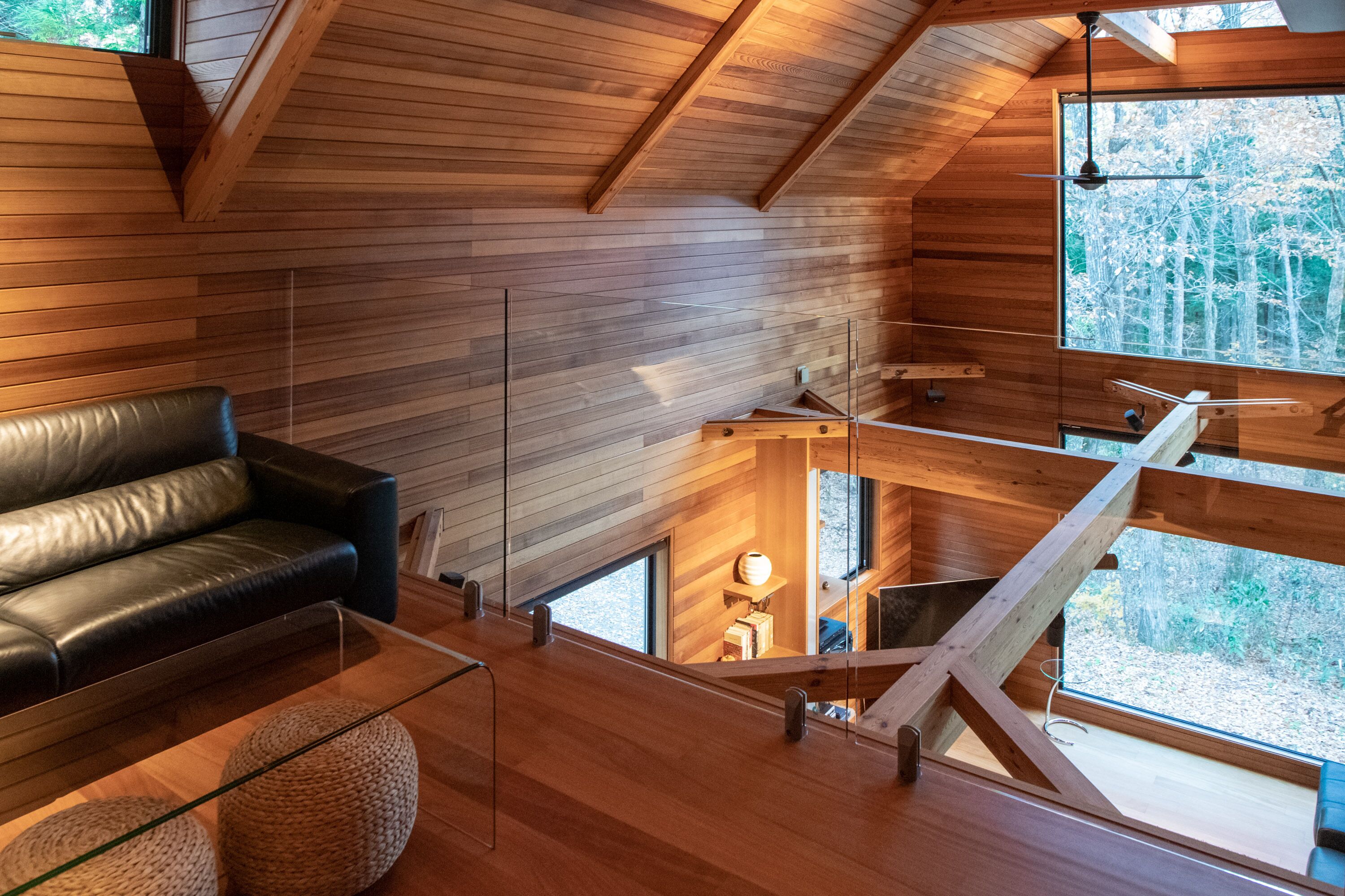 A modern loft-style room with a wooden ceiling, a black leather couch, and a glass table.