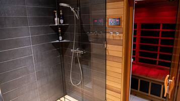 A modern shower area with a digital control panel, a glass-enclosed shower, and a wooden door leading to a red-lit room.
