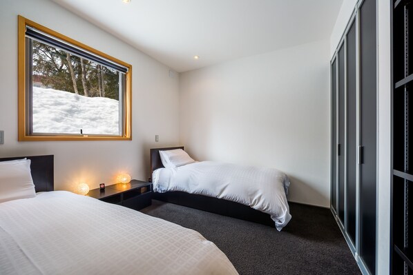 A modern hotel room with two beds, a large window with a view of a snowy landscape, and a wardrobe with sliding doors. - Phoenix Chalets (Hakuba)