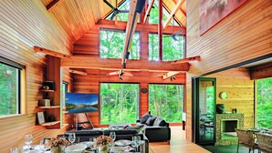 A spacious, modern cabin with a high ceiling, large windows, and a cozy living area with a fireplace. - Phoenix Chalets (Hakuba)
