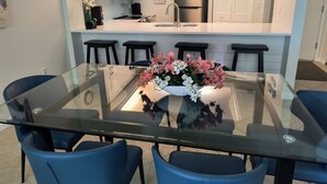 A modern kitchen with white cabinets, a stainless steel refrigerator, and a glass dining table with blue chairs. - Oceanfront/Beachfront -Sarasota Surf  Racquet - Y Building (Sarasota)