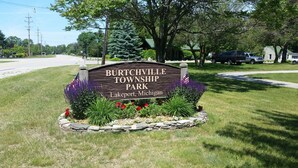 A sign for Burchtville Township Park in Lakeport, Michigan, surrounded by a stone border and flowering plants.