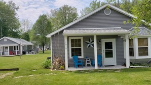 A small, single-story cabin with a porch, numbered 975, surrounded by a grassy yard and trees.