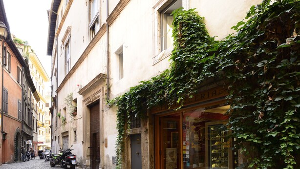 A narrow cobblestone street with buildings on either side, one with a shop entrance and another with a motorcycle parked outside. - Close To Piazza Navona, Historic, Charming & Romantic Flat, 2 Bath, AC, Wi-Fi (Roma)
