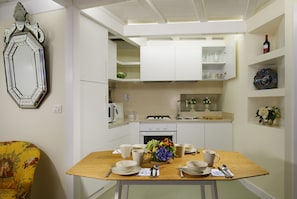 A compact kitchen with white cabinets, a dining table set with white dishes, and a mirror on the wall.