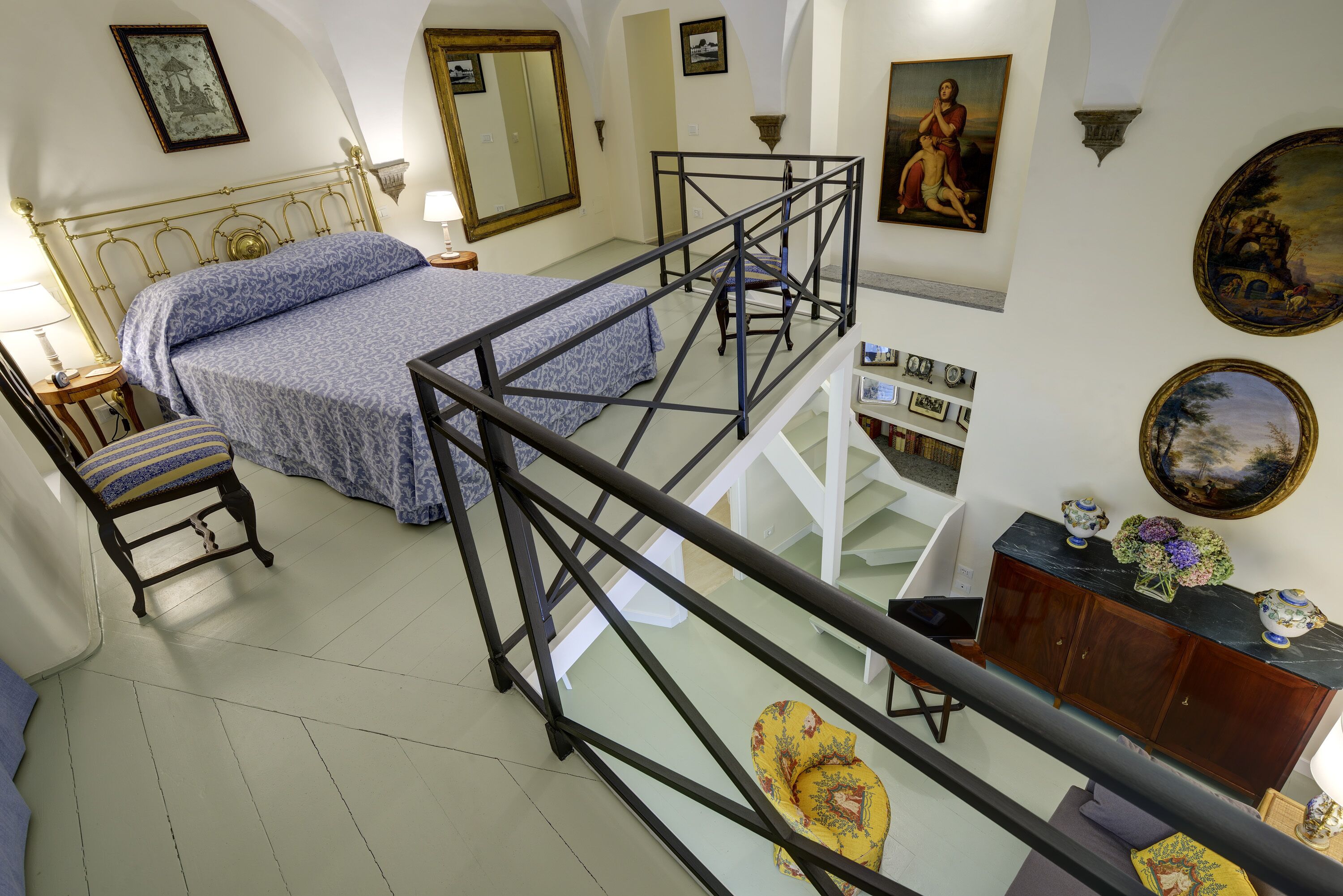 Una camera da letto con un letto, una sedia, una scrivania, una scala e una parete con quadri.