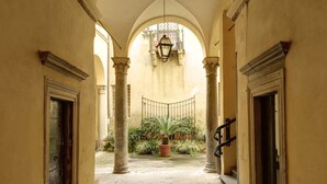 A corridor with arches, columns, and a tiled floor leading to a courtyard with plants and a hanging light fixture. - Close To Piazza Navona, Historic, Charming & Romantic Flat, 2 Bath, AC, Wi-Fi (Roma)