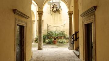 Un corridoio con archi, colonne e pavimento piastrellato che conduce a un cortile con piante e un lampadario.