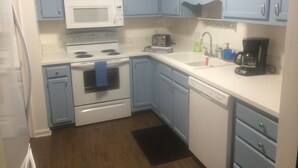 A kitchen with blue cabinets, a white microwave, a stove, a toaster, and a coffee maker.