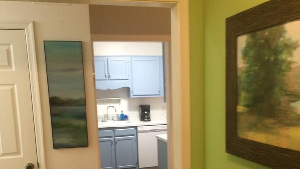 A hallway leading to a kitchen with light blue cabinets, a dishwasher, and a coffee maker.