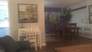 A living room with a sofa, a dining table with chairs, a painting on the wall, and a plant.