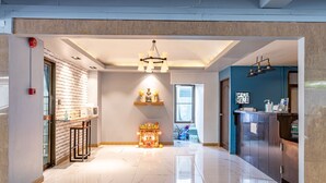 A modern hotel lobby with a marble floor, a central decorative light fixture, a reception desk, and a blue accent wall. - Living Naraa Place (Bangkok)
