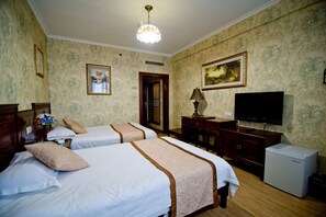 A hotel room with two beds, a television, a small refrigerator, and a lamp.