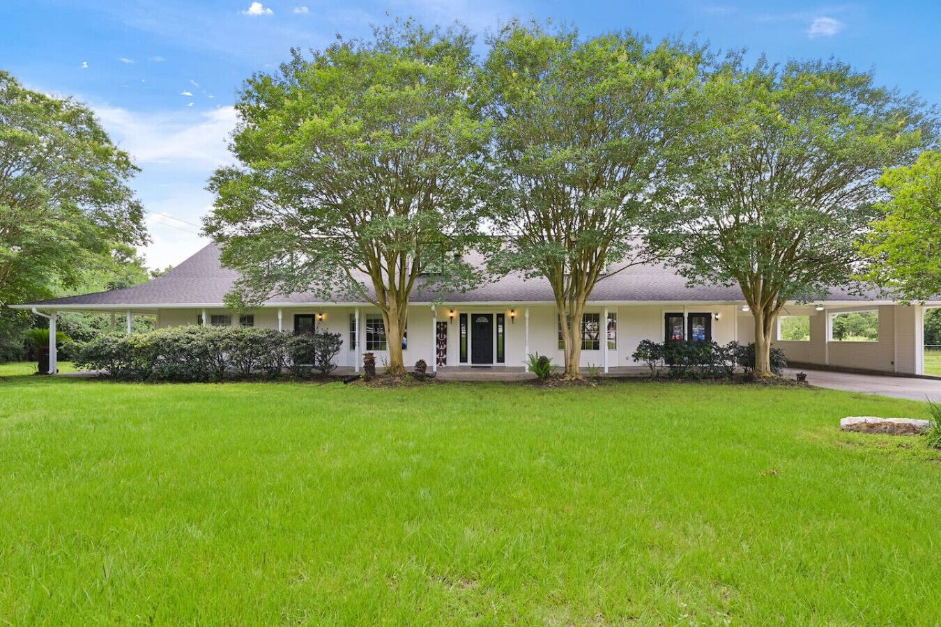 A single-story house with a covered porch, a front lawn, and mature trees.