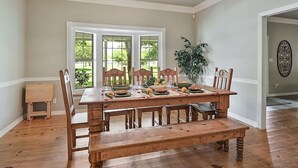 A dining room with a wooden table set for four, large windows, a plant, and a decorative wall piece. - Rambling Ranch ~ The Ultimate Gathering Place! (College Station)