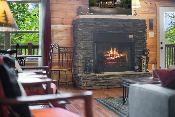 A cozy cabin interior with a stone fireplace, wooden furniture, and a view of the outdoors. - Prime Gatlinburg Mountain Log Cabin*hot tub*game room* romance*honeymooners (Gatlinburg)