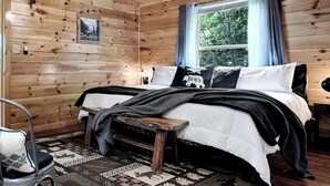 Un dormitorio de cabaña de madera con una cama, un banco, una silla y una ventana con cortinas.