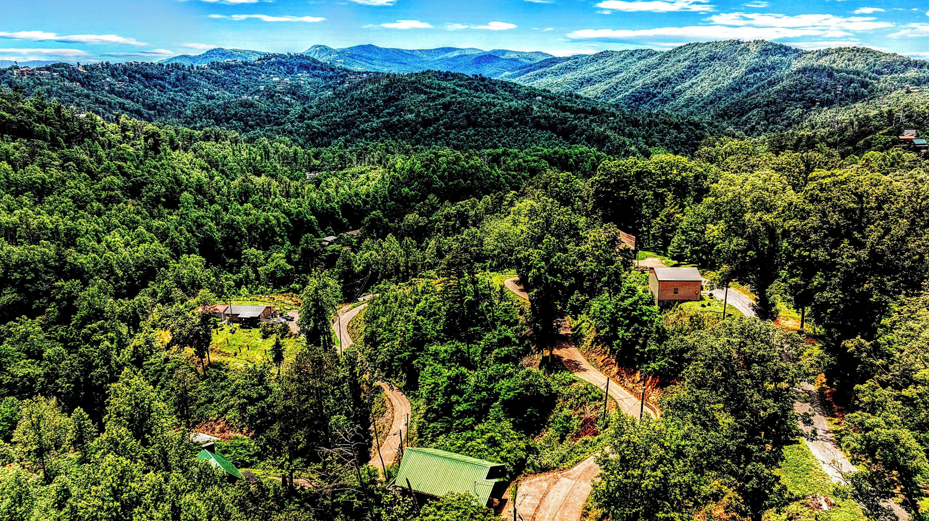 A mountainous landscape with dense forests, a winding road, and several buildings.