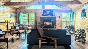 Interior acogedor de una cabaña con chimenea, paredes de madera y televisor montado encima.
