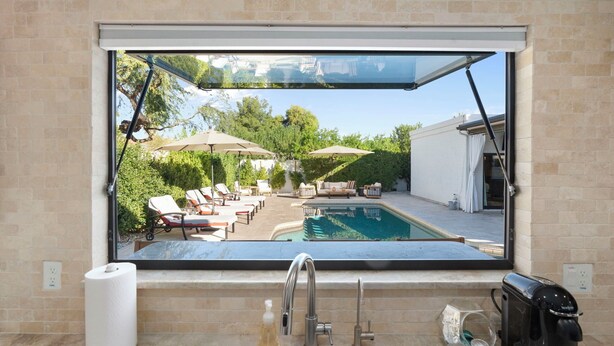 A bathroom with a large window overlooking a pool area, a sink, and a coffee maker.