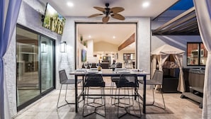 An outdoor dining area with a table set for four, surrounded by chairs, and a ceiling fan above.