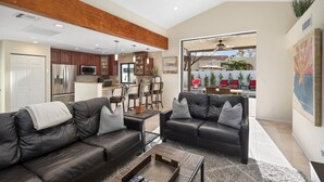 A modern living room with a black leather sofa, a coffee table, and a view of the backyard.
