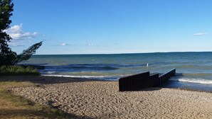 A beach with a wooden walkway leading to the water, pebbles, and a clear sky. - The Beach House Cottage (Fort Gratiot Twp)