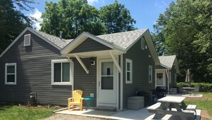 A small, single-story cabin with a porch, a table, and a chair. - The Beach House Cottage (Fort Gratiot Twp)