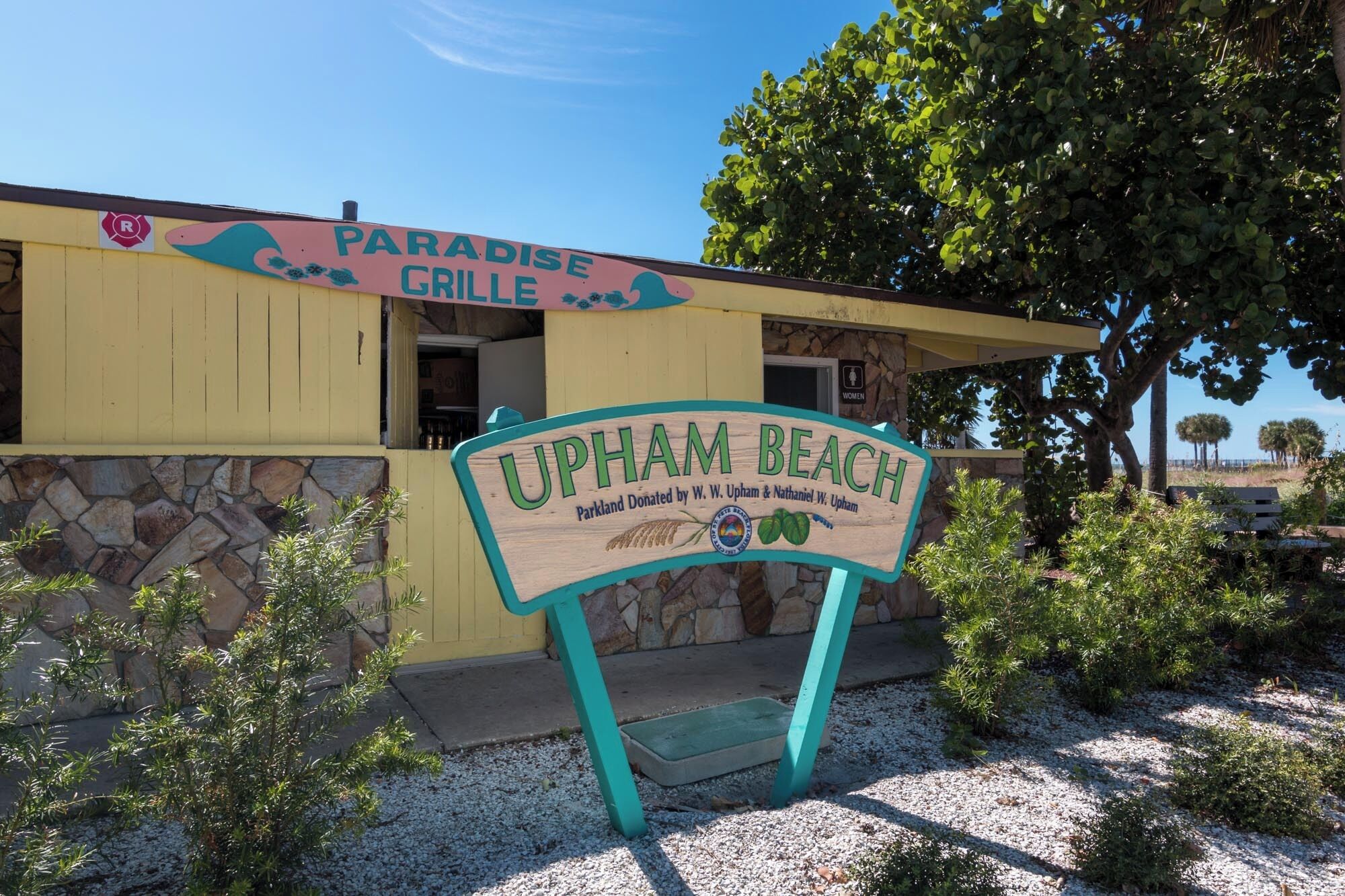 A building with a sign reading "Paradise Grille" and another sign stating "Upham Beach".