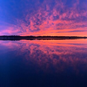 Un lago tranquillo che riflette un cielo al tramonto con sfumature rosa e viola.