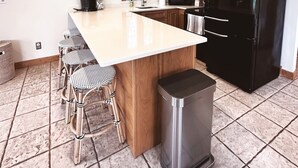 A modern kitchen with wooden cabinets, a black refrigerator, a stainless steel trash bin, and a bar stool area. - Door county cottage (Sturgeon Bay)