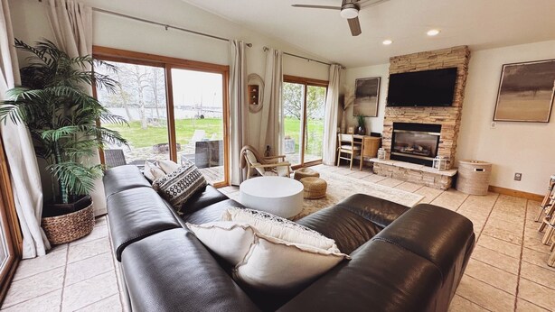 A spacious living room with a fireplace, leather sofas, a dining area, and a large window offering a view of the outdoors. - Door county cottage (Sturgeon Bay)