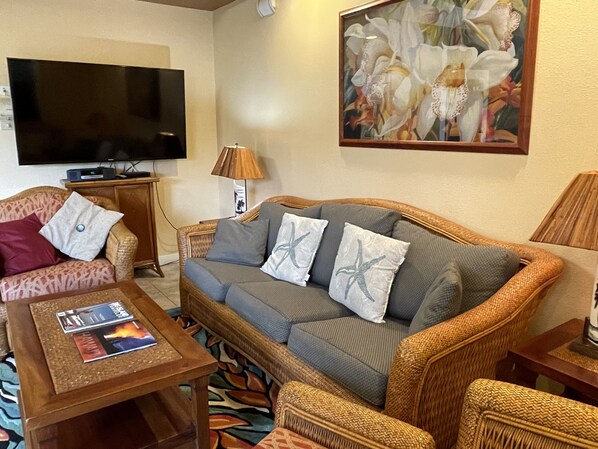 A living room with a sofa, a coffee table, a television, and a painting. - Beach Front Condo (Ocean View), Best Snorkeling/Surfing. (Kailua-Kona)