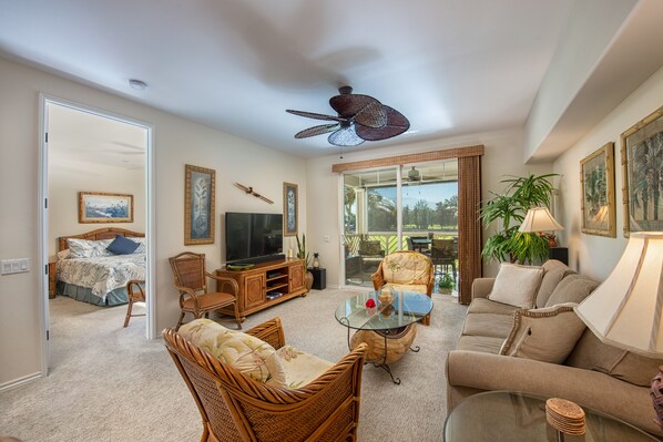 A living room with a sofa, chairs, a glass coffee table, a television, and a ceiling fan. - Waikoloa Easy Walk to Beach, Golf Views (Waikoloa)