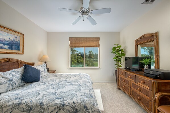 A bedroom with a bed, a ceiling fan, a window with a view, a dresser, and a television. - Waikoloa Easy Walk to Beach, Golf Views (Waikoloa)