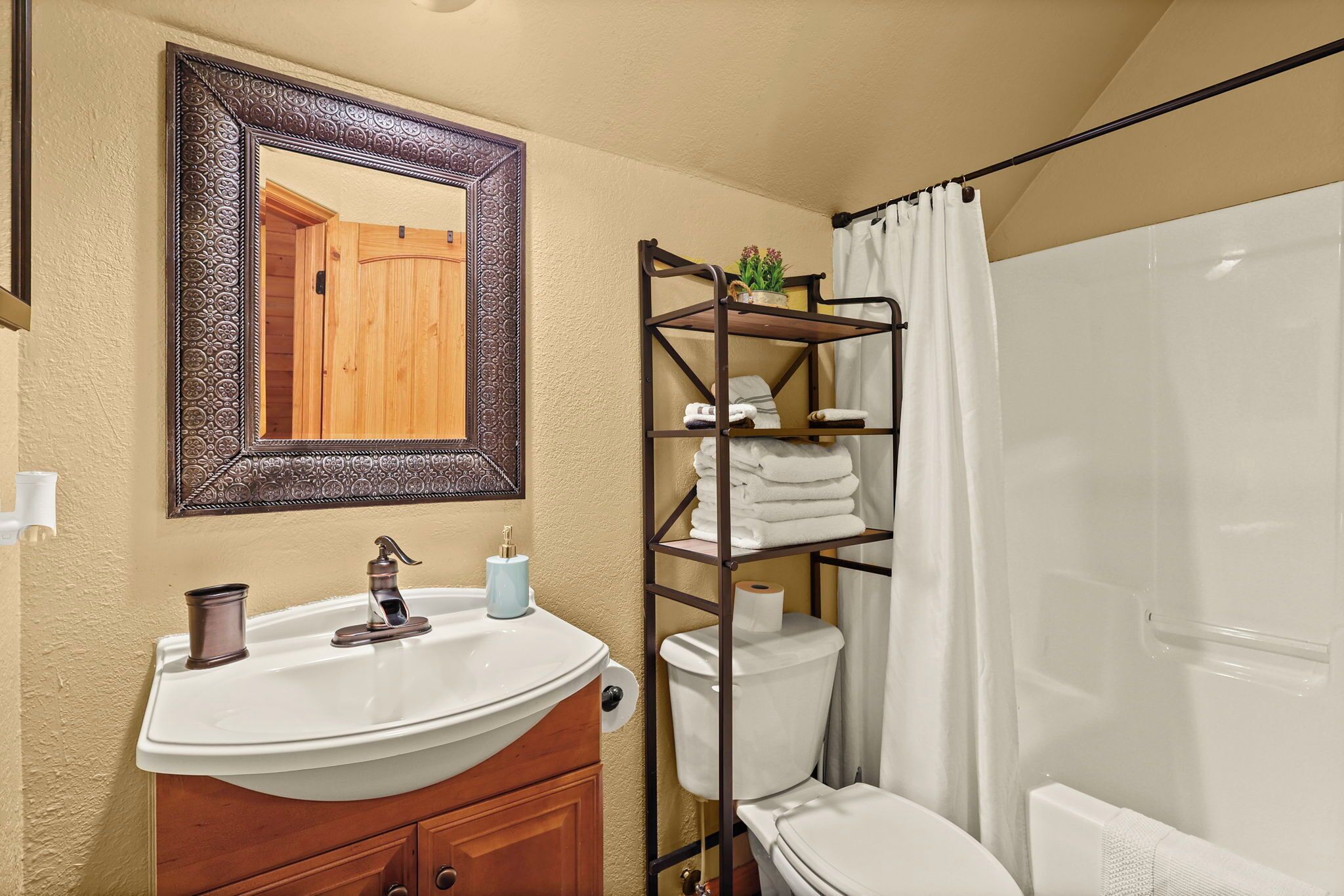 Un baño con tocador de madera, lavamanos, espejo, inodoro y cortina de ducha.