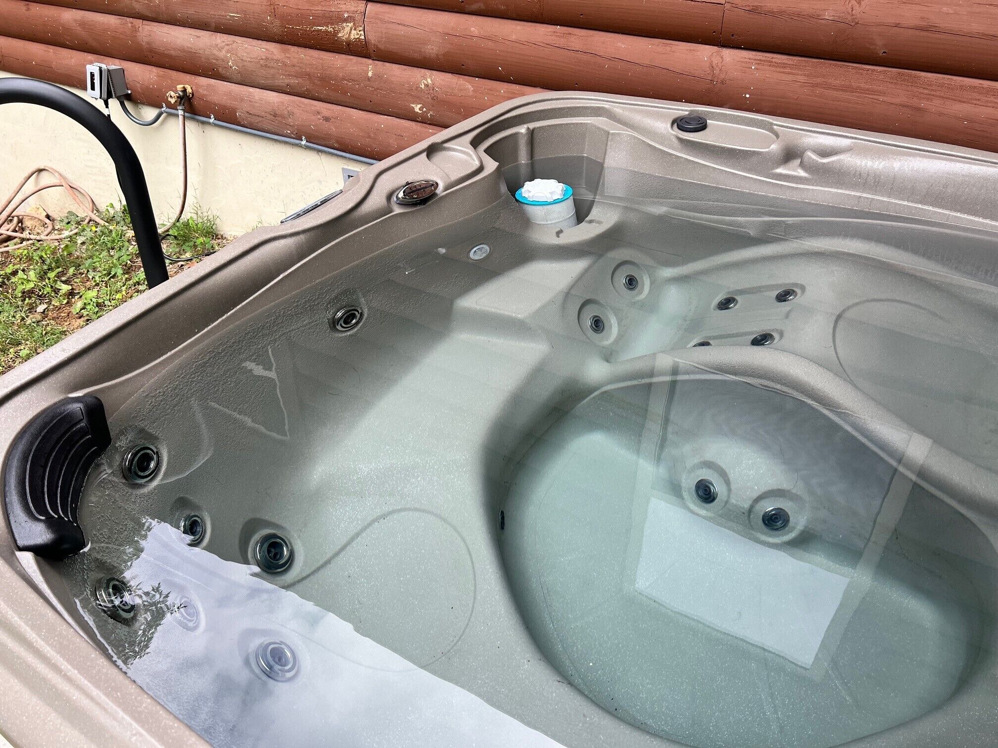 A hot tub with a clear glass cover, a control panel, and a hose connected to an electrical outlet.